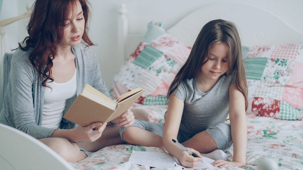 Mutter und Tochter stärken ihre Bindung beim Lesen und Schreiben auf einem gemütlichen Bett.